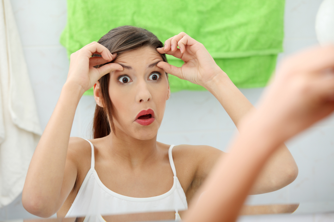 Shocked young woman checking her wrinkles on her forehead at bathroom