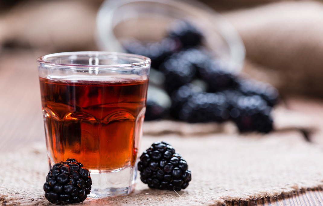 Blackberry Liqueur shot (with some fresh fruits) on wooden background